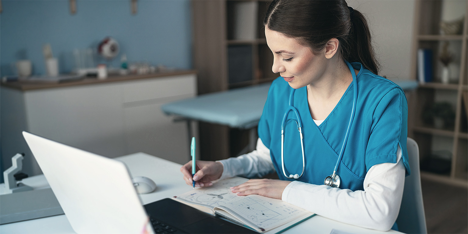 Female doctor writing notes and using laptop
